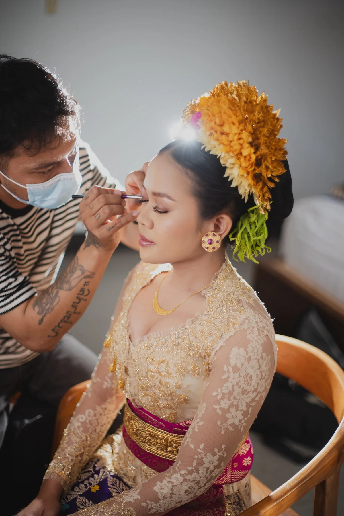 Agus applying eye makeup to a bride wearing ivory lace and gold floral hair accessories